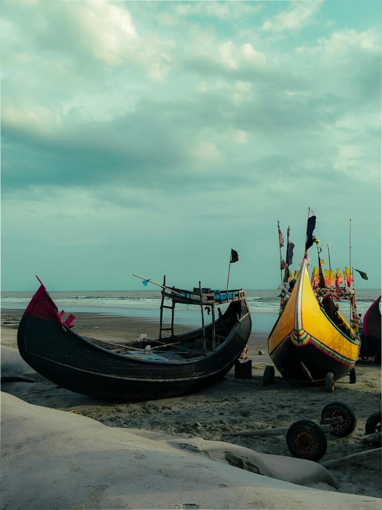 Colorful fishing boats rest on the serene Cox's Bazar beach in Bangladesh under a cloudy sky.
